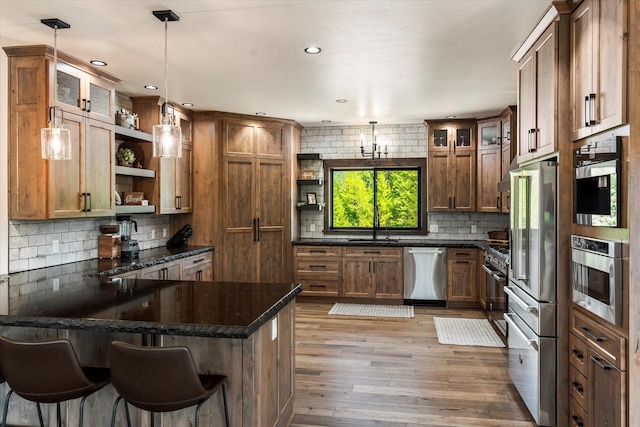 kitchen with pendant lighting, appliances with stainless steel finishes, dark stone counters, light hardwood / wood-style floors, and a breakfast bar