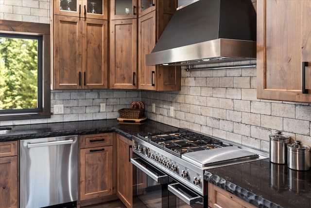 kitchen with stainless steel appliances, tasteful backsplash, dark stone counters, and wall chimney range hood