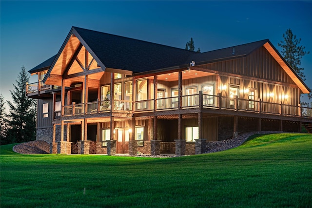 back house at dusk featuring a balcony and a lawn