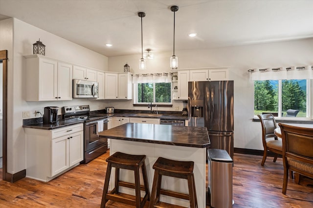 kitchen with white cabinetry, hardwood / wood-style flooring, appliances with stainless steel finishes, decorative light fixtures, and a center island