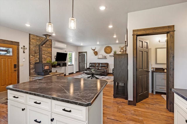 kitchen with white cabinetry, a wall unit AC, a wood stove, pendant lighting, and a center island