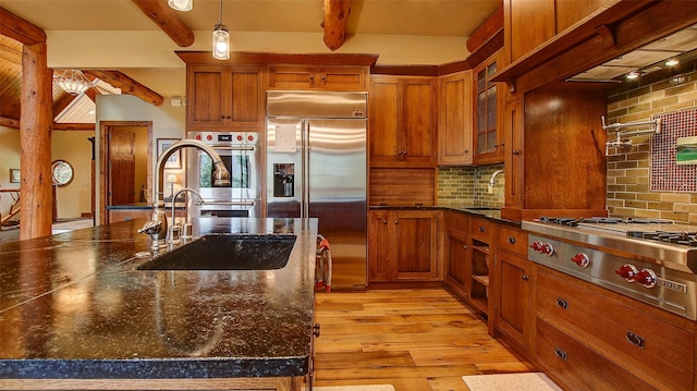 kitchen featuring decorative backsplash, appliances with stainless steel finishes, sink, dark stone countertops, and beamed ceiling