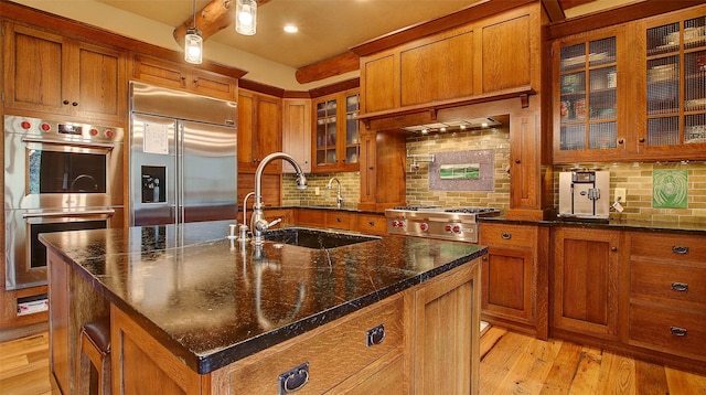 kitchen with sink, stainless steel appliances, tasteful backsplash, a center island with sink, and light wood-type flooring