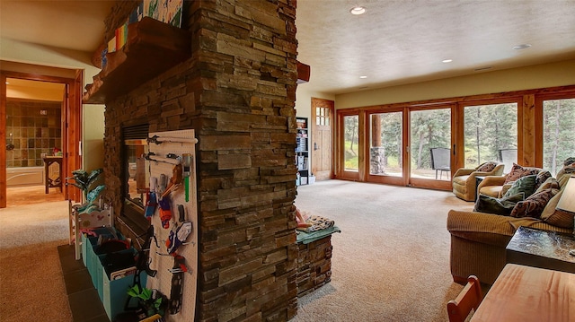 living room with a stone fireplace, carpet, and a textured ceiling