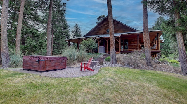 rear view of property featuring a patio, a yard, and a hot tub