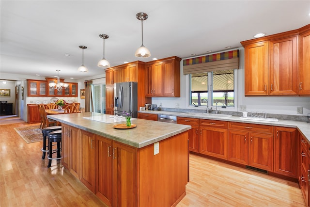 kitchen with stainless steel appliances, sink, hanging light fixtures, light hardwood / wood-style floors, and a center island