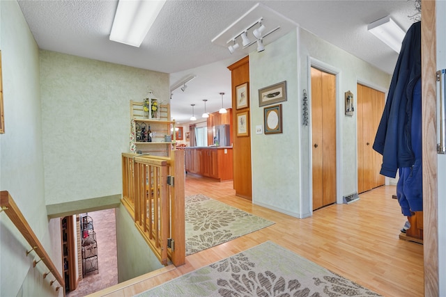 corridor with light hardwood / wood-style flooring, a textured ceiling, and rail lighting