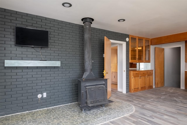 unfurnished living room with hardwood / wood-style floors, brick wall, and a wood stove