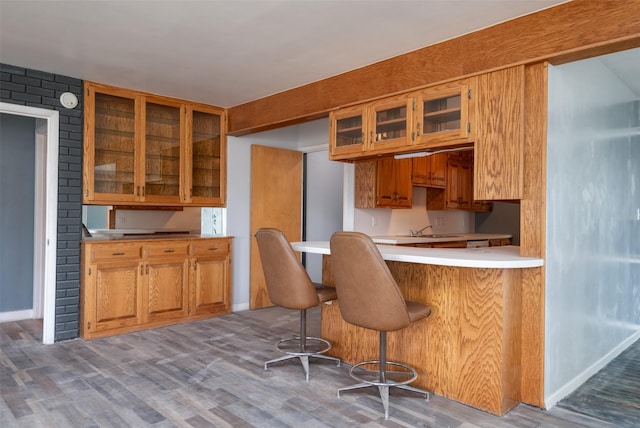 kitchen featuring brick wall, sink, a kitchen bar, kitchen peninsula, and light hardwood / wood-style flooring