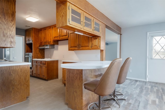 kitchen with light hardwood / wood-style floors, kitchen peninsula, stainless steel oven, and a kitchen bar