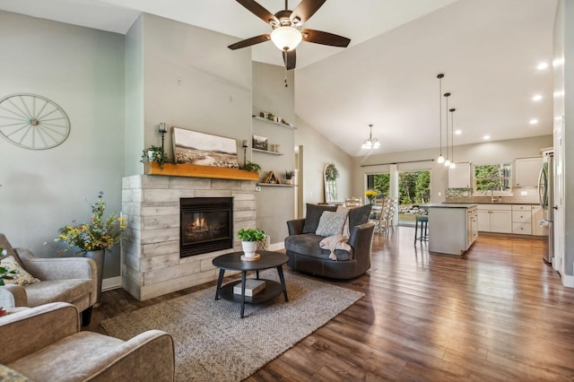 living room featuring sink, ceiling fan with notable chandelier, high vaulted ceiling, wood-type flooring, and a stone fireplace