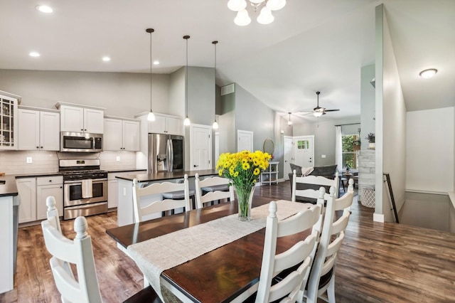 dining space with high vaulted ceiling, dark hardwood / wood-style flooring, and ceiling fan with notable chandelier