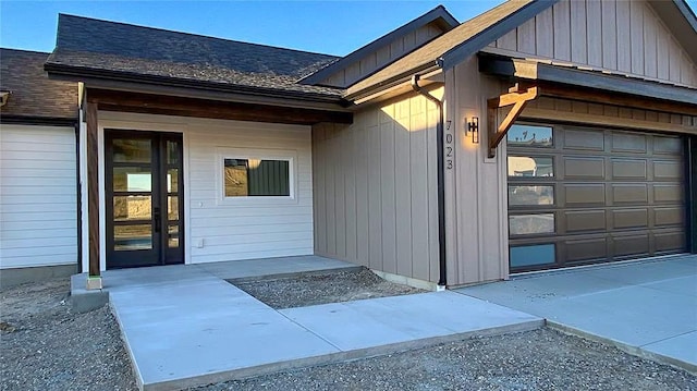 entrance to property with board and batten siding, roof with shingles, and an attached garage