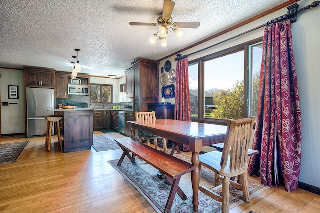 dining area featuring light wood-type flooring, a textured ceiling, ceiling fan, and crown molding