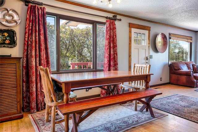 dining area featuring a textured ceiling, plenty of natural light, light wood-type flooring, and ornamental molding