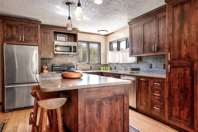 kitchen featuring stainless steel appliances, hanging light fixtures, light wood-type flooring, and a center island