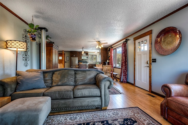 living room featuring ceiling fan, a textured ceiling, light hardwood / wood-style floors, and crown molding