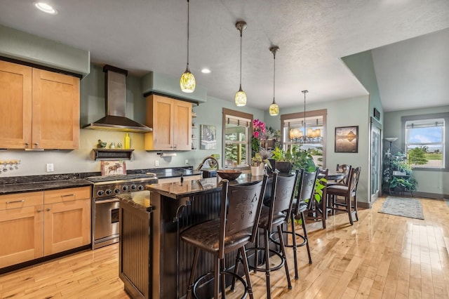 282 Mcwenneger Dr, Kalispell, MT 59901 - kitchen featuring wall chimney range hood, stainless steel range, light wood-style flooring, a kitchen island, and a breakfast bar