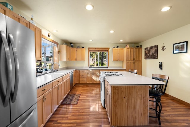 kitchen with sink, a center island, dark hardwood / wood-style floors, a breakfast bar, and appliances with stainless steel finishes