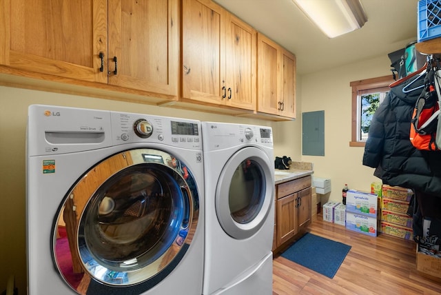 laundry room with washing machine and clothes dryer, electric panel, light hardwood / wood-style flooring, and cabinets