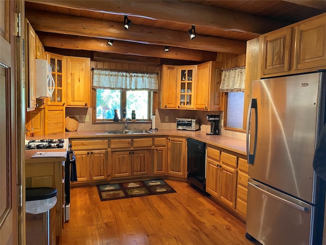 kitchen featuring stainless steel refrigerator, beamed ceiling, black dishwasher, hardwood / wood-style flooring, and sink