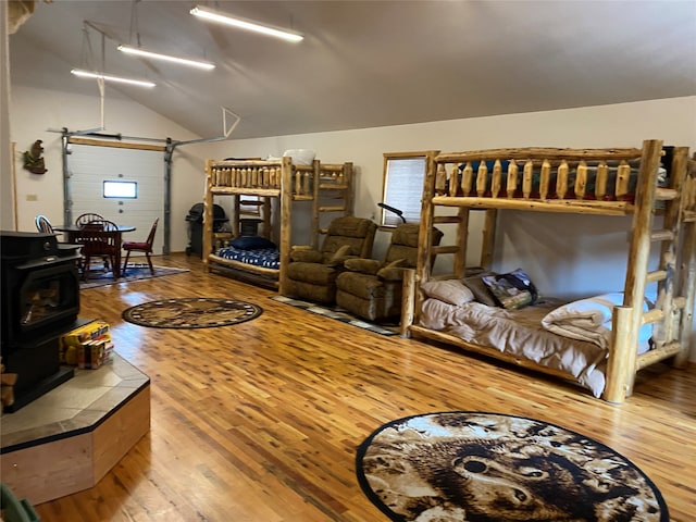 bedroom featuring vaulted ceiling, hardwood / wood-style floors, and a wood stove