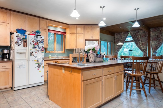 kitchen with pendant lighting, sink, white appliances, a center island with sink, and light brown cabinetry