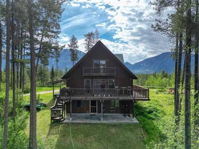 rear view of property with a balcony, a deck with mountain view, a patio, and a yard