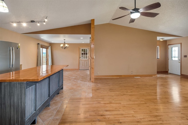 kitchen with butcher block counters, decorative light fixtures, vaulted ceiling, a breakfast bar area, and ceiling fan with notable chandelier