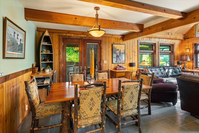 tiled dining space with beam ceiling, french doors, and wooden walls