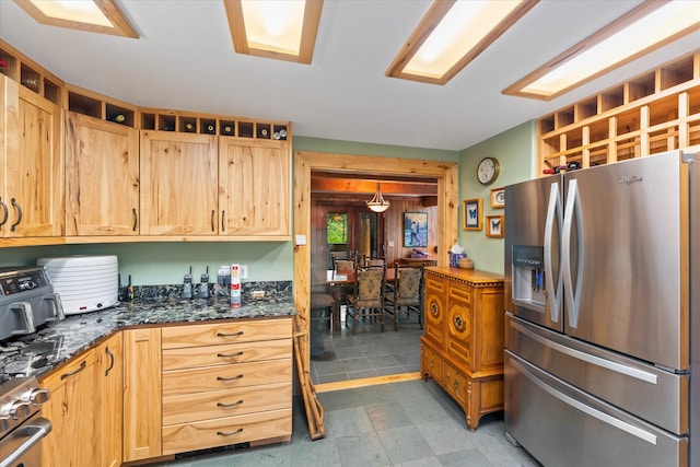 kitchen featuring stainless steel fridge with ice dispenser, range, dark stone counters, and light tile patterned floors