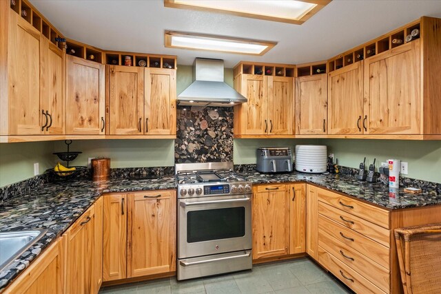 kitchen featuring dark stone counters, wall chimney range hood, high end stainless steel range oven, sink, and light tile patterned floors