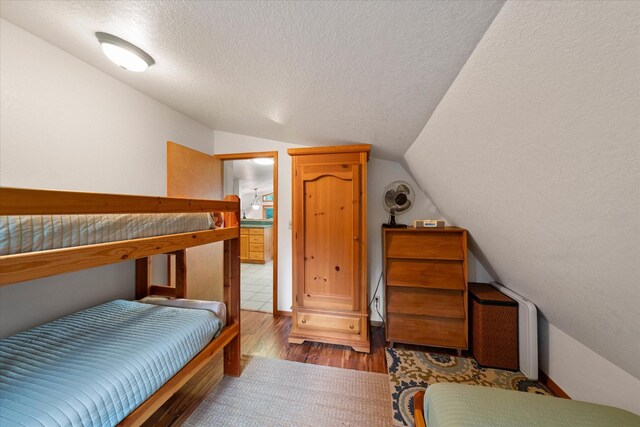 bedroom with dark wood-type flooring, lofted ceiling, and a textured ceiling