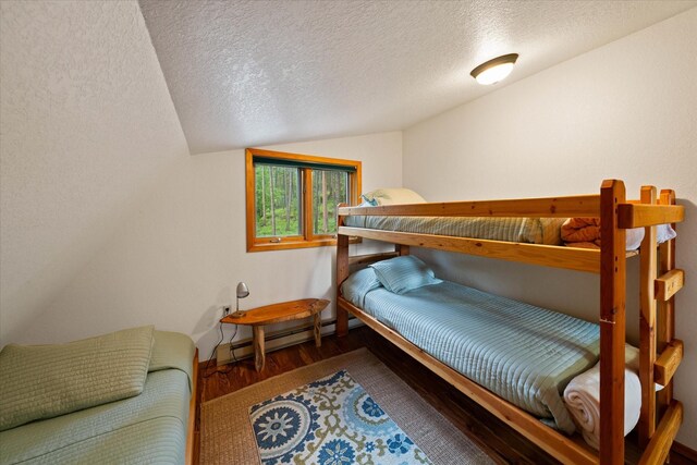 bedroom featuring dark hardwood / wood-style floors, lofted ceiling, baseboard heating, and a textured ceiling