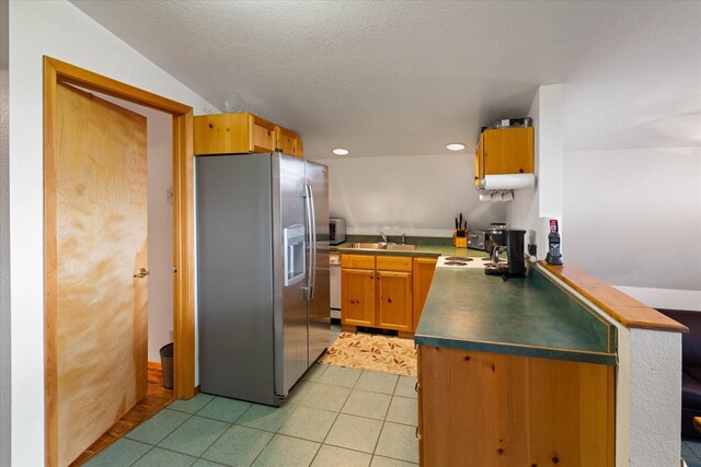 kitchen featuring light tile patterned floors, a textured ceiling, kitchen peninsula, appliances with stainless steel finishes, and sink