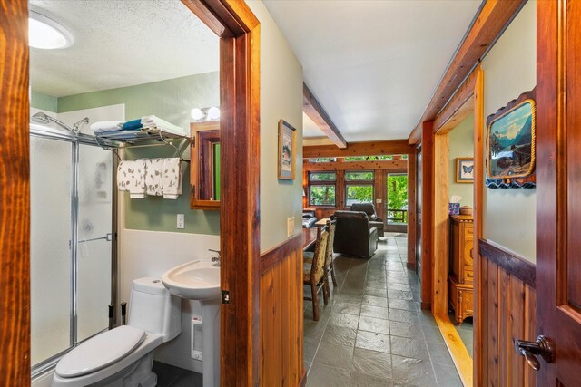 bathroom featuring a shower with shower door, beamed ceiling, tile patterned flooring, a textured ceiling, and toilet