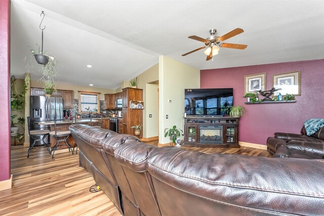 living room with sink, vaulted ceiling, a fireplace, light hardwood / wood-style flooring, and ceiling fan