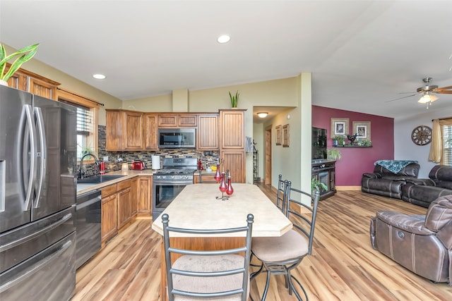 kitchen with ceiling fan, sink, appliances with stainless steel finishes, light wood-type flooring, and vaulted ceiling