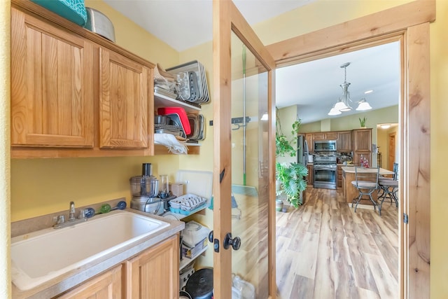 kitchen with stainless steel appliances, a sink, light countertops, light wood finished floors, and pendant lighting