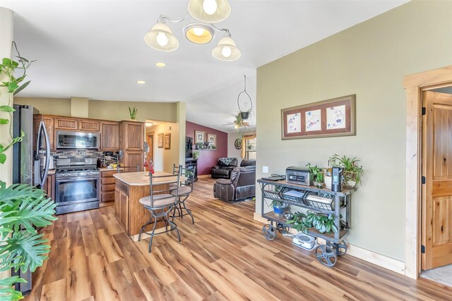 kitchen featuring lofted ceiling, decorative light fixtures, appliances with stainless steel finishes, ceiling fan with notable chandelier, and light hardwood / wood-style floors