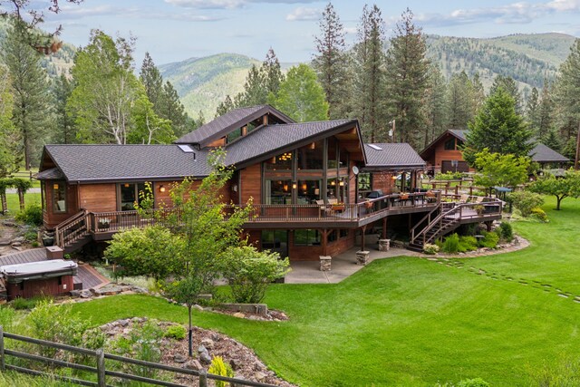 rear view of house featuring a deck with mountain view, a patio area, a lawn, and a hot tub