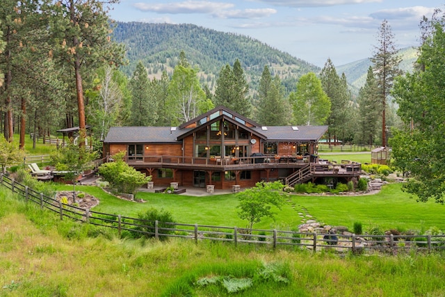 back of property featuring a deck with mountain view, a lawn, and a rural view