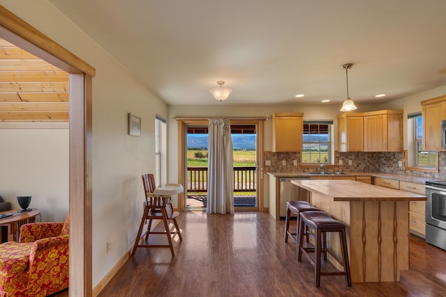 kitchen featuring tasteful backsplash, decorative light fixtures, light brown cabinetry, a kitchen island, and appliances with stainless steel finishes