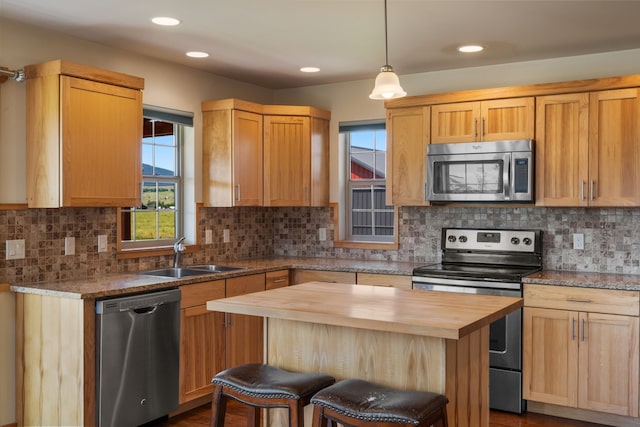 kitchen with sink, appliances with stainless steel finishes, butcher block countertops, a kitchen island, and a breakfast bar area