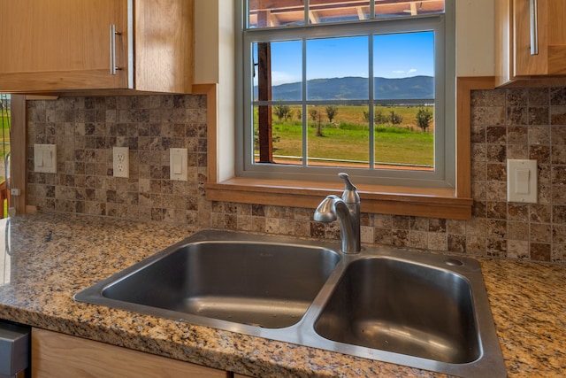 room details featuring a mountain view, light stone counters, sink, and tasteful backsplash