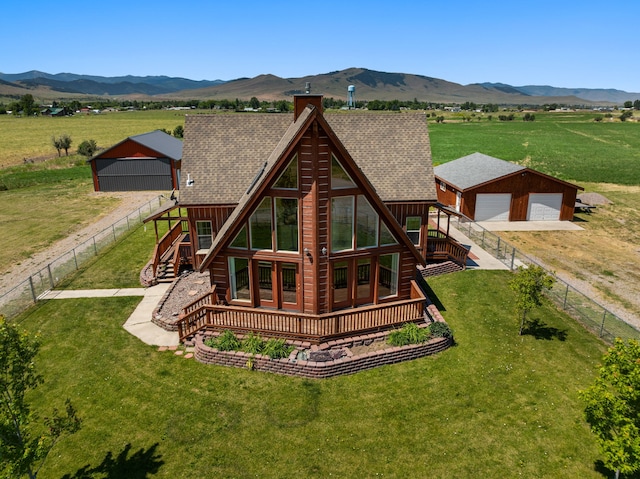 back of house featuring an outbuilding, a rural view, a deck with mountain view, a garage, and a lawn