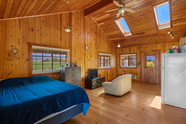 bedroom featuring a skylight, beamed ceiling, white refrigerator, wood walls, and light wood-type flooring