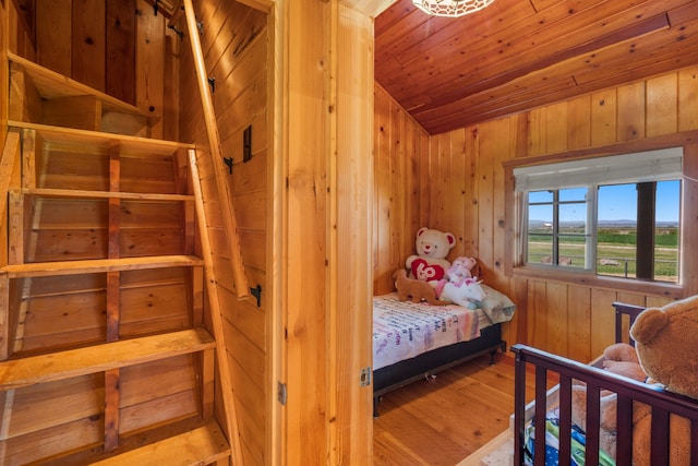 bedroom with vaulted ceiling, light hardwood / wood-style flooring, wooden ceiling, and wood walls