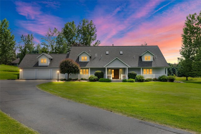 new england style home featuring a garage, a porch, and a lawn