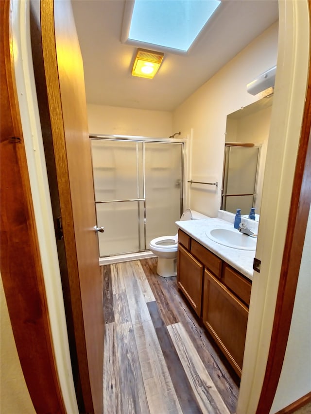 bathroom featuring a skylight, vanity, wood-type flooring, a shower with shower door, and toilet